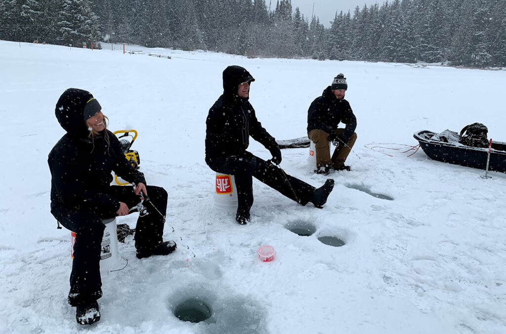 Three people sit on an icy lake, fishing in the winter in Whistler.