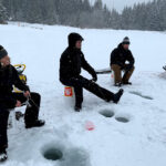Three people sit on an icy lake, fishing in the winter in Whistler.