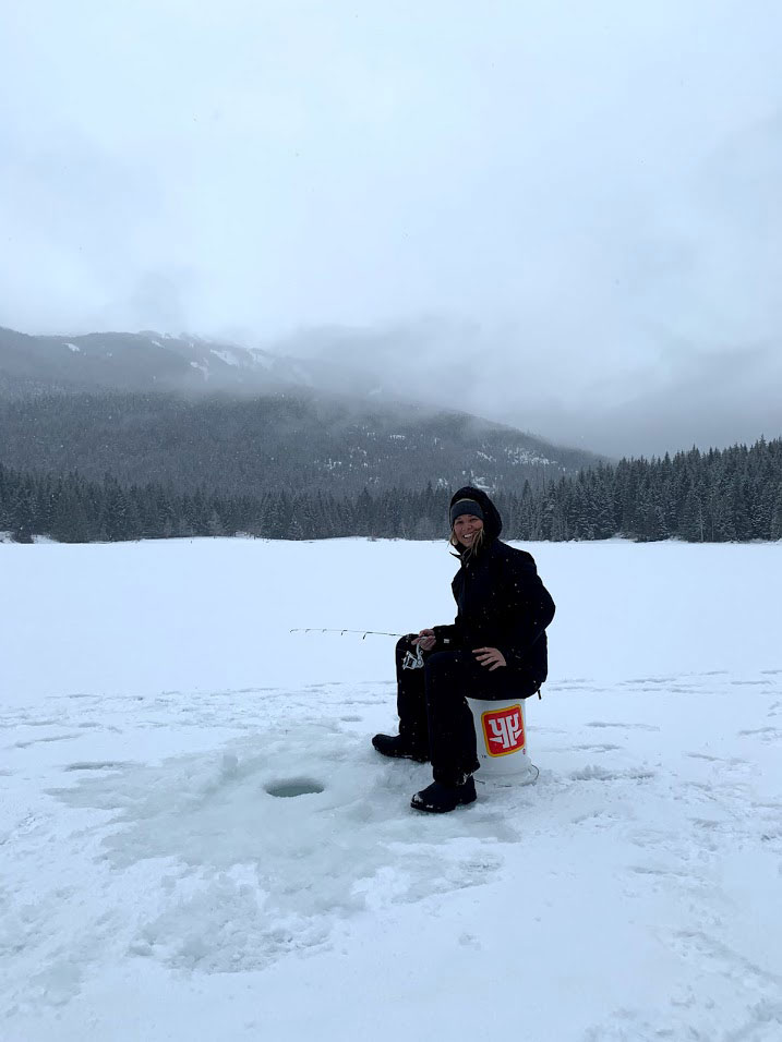 A person sits over a hole in an iced-over lake waiting for a fish to bite.