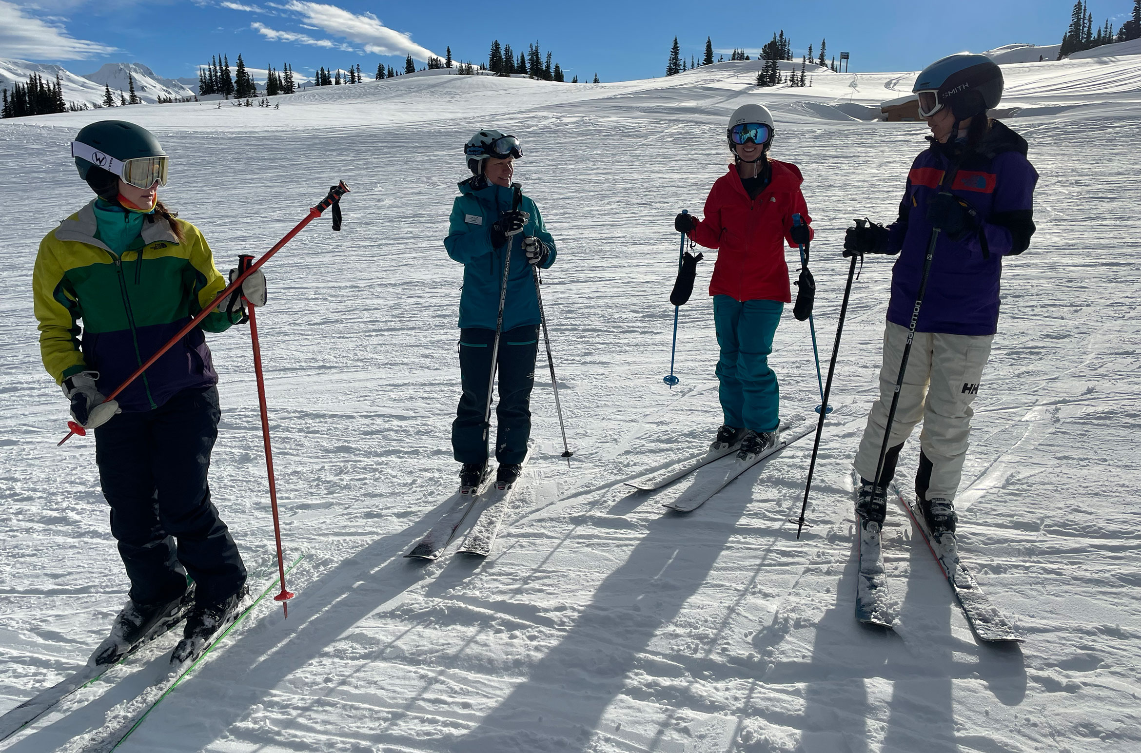 Four skiers stop on a slope in the sun for some instruction from their coach.