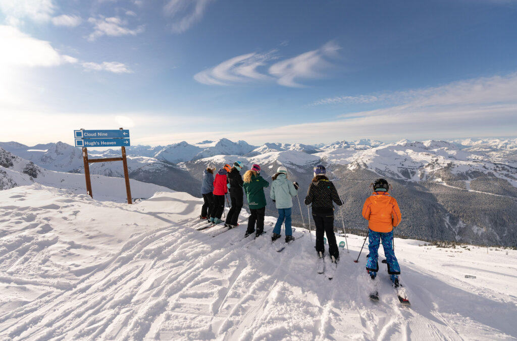 A group of skiers stand on the ridge of a run assessing the terrain below.