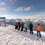 A group of skiers stand on the ridge of a run assessing the terrain below.