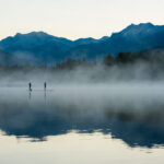 Paddle boarders on a lake in Whistler with the morning mist.