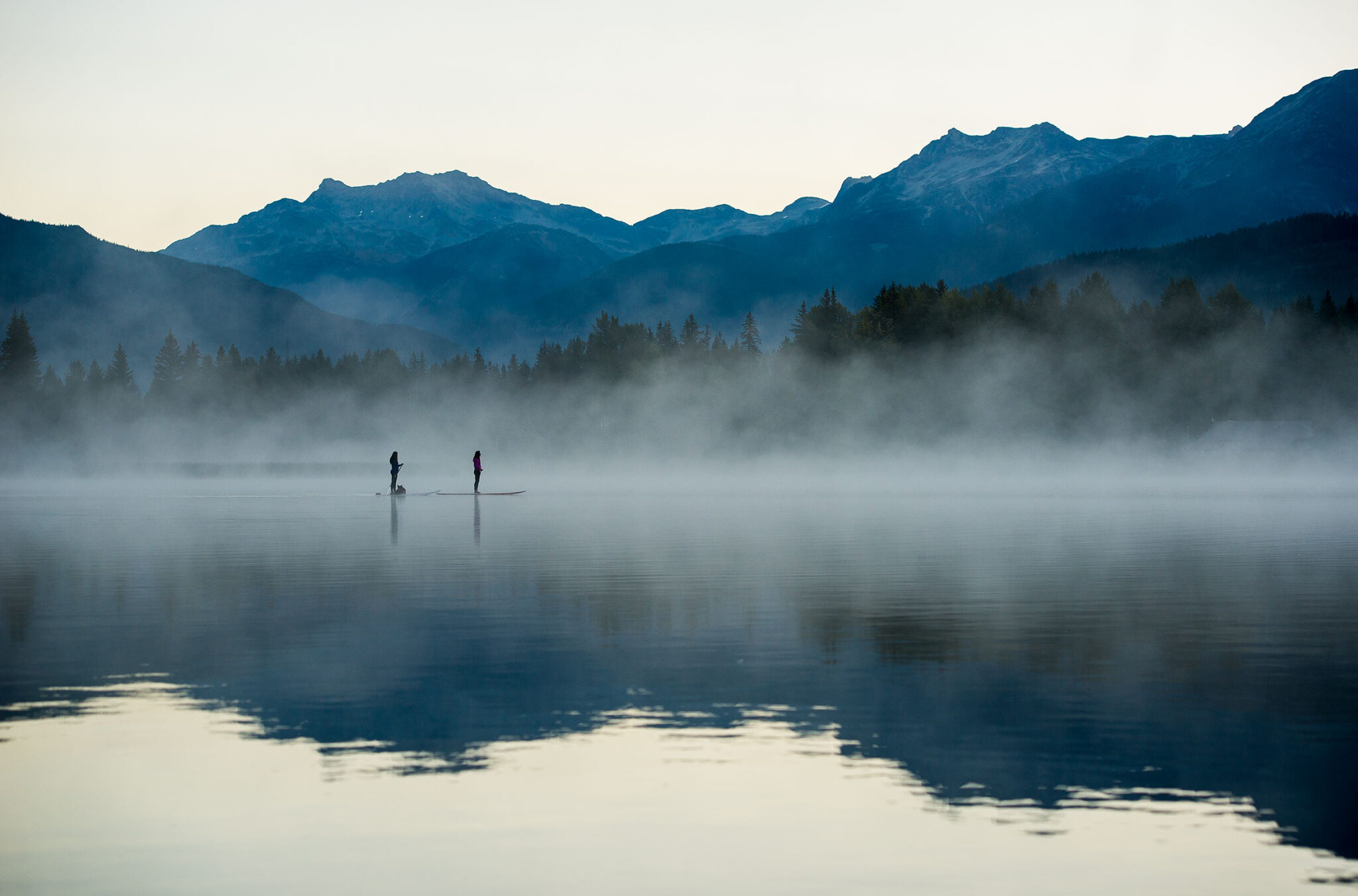 Paddle boarders on a lake in Whistler with the morning mist.