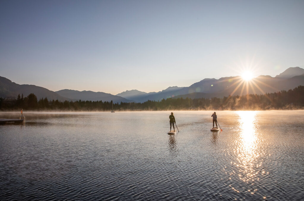 Two paddle boarders enjoy the mountains and morning sun on a lake in Whistler. 