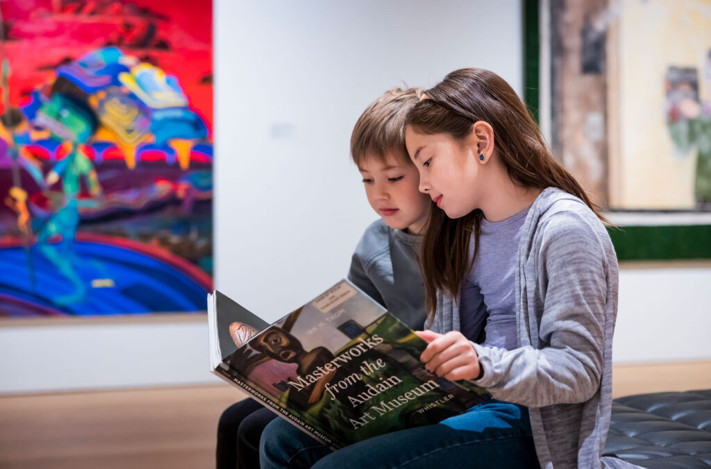 Two young children read an art book while they're surrounded by works of art at the Audain Art Museum in Whistler.