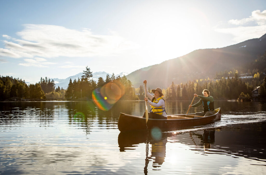 Two people canoe on a lake in Whistler in the morning sunshine.