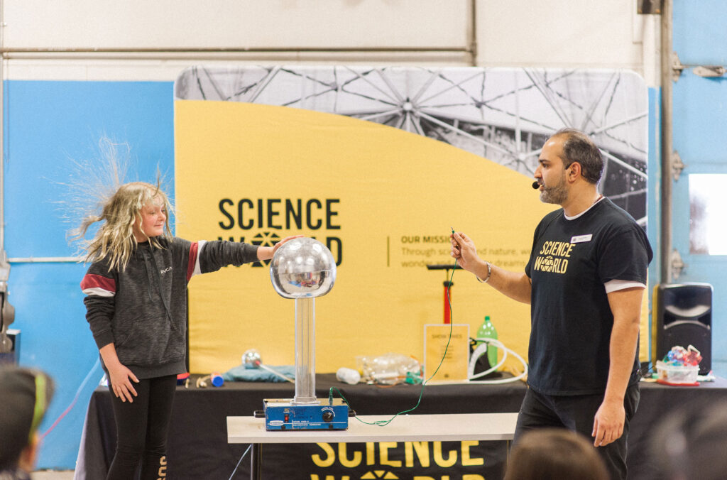 A Science World demonstration has a young girl placing her hand on a plasma orb and her hair is standing on end.