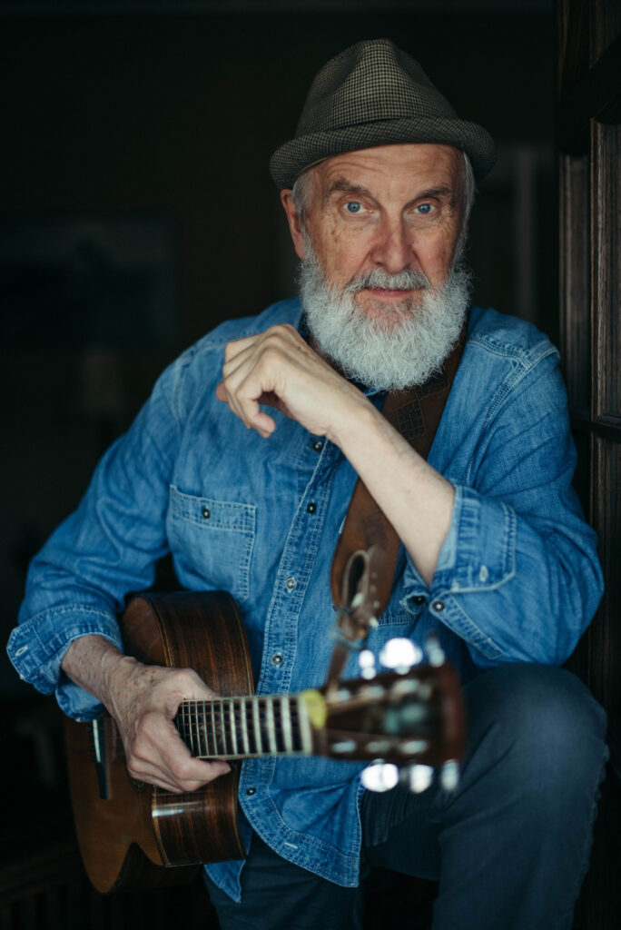 Performer and musician Fred Penner looks at the camera with his guitar in hand. 