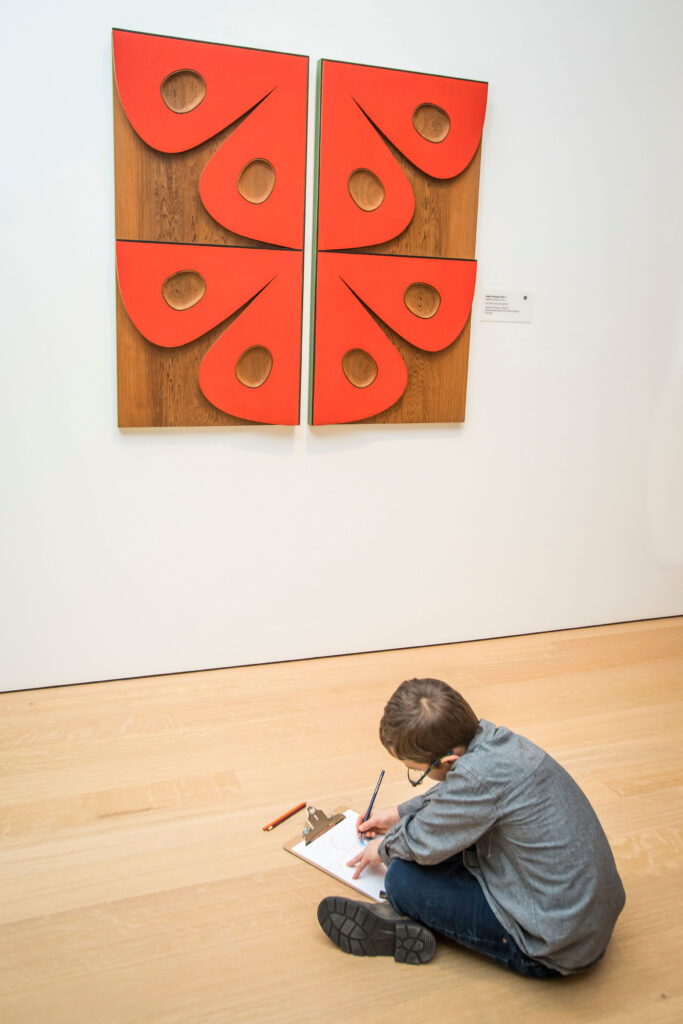 A young boy sketches in a pad while looking at art at the Audain Art Museum.