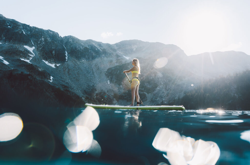 A woman paddleboards on a glittering alpine lake, only accessed by helicopter. This definitely puts the adventure in adventure dining.