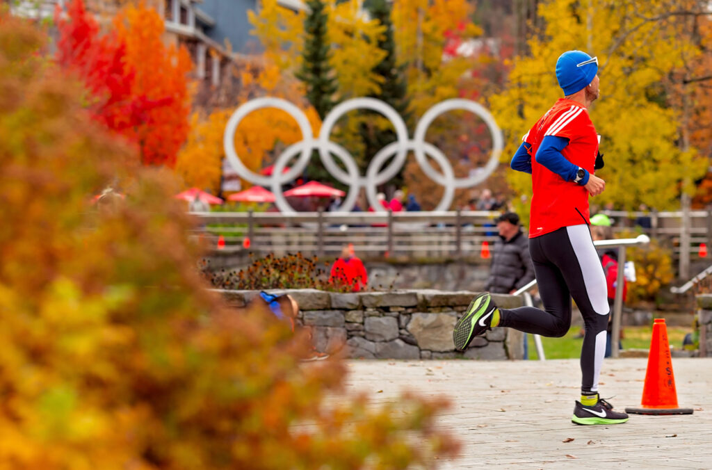 A runner in the Whistler 50 Ultra heads to the finish line with the Olympic rings and fall colours as their backdrop.