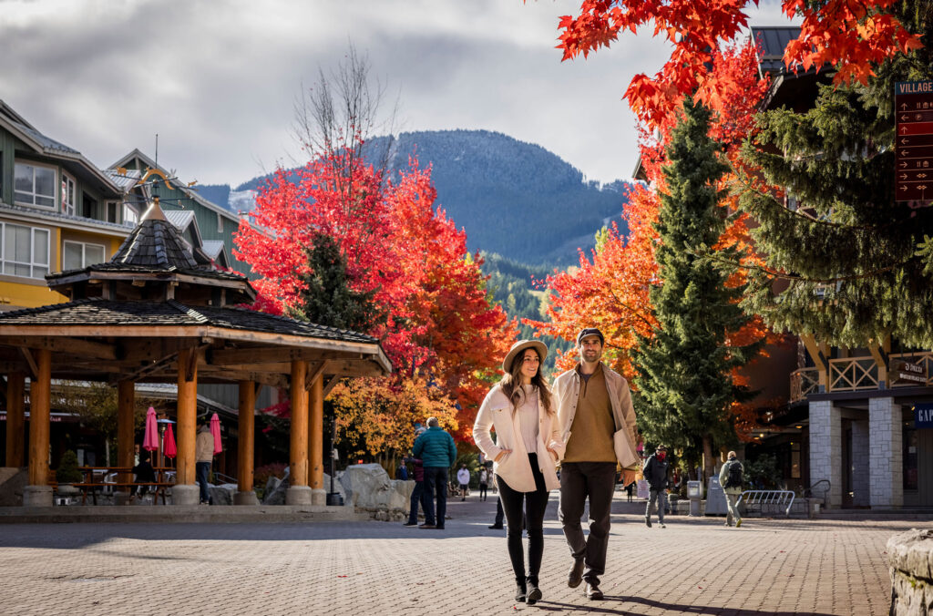 A couple walk through the Whistler Village Stroll with the fall colours around them.