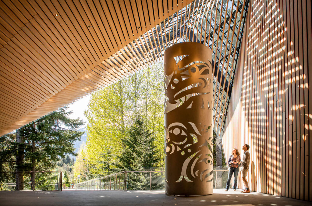 A couple look up at the artwork outside the Audain Art Museum in the fall sunshine in Whistler.