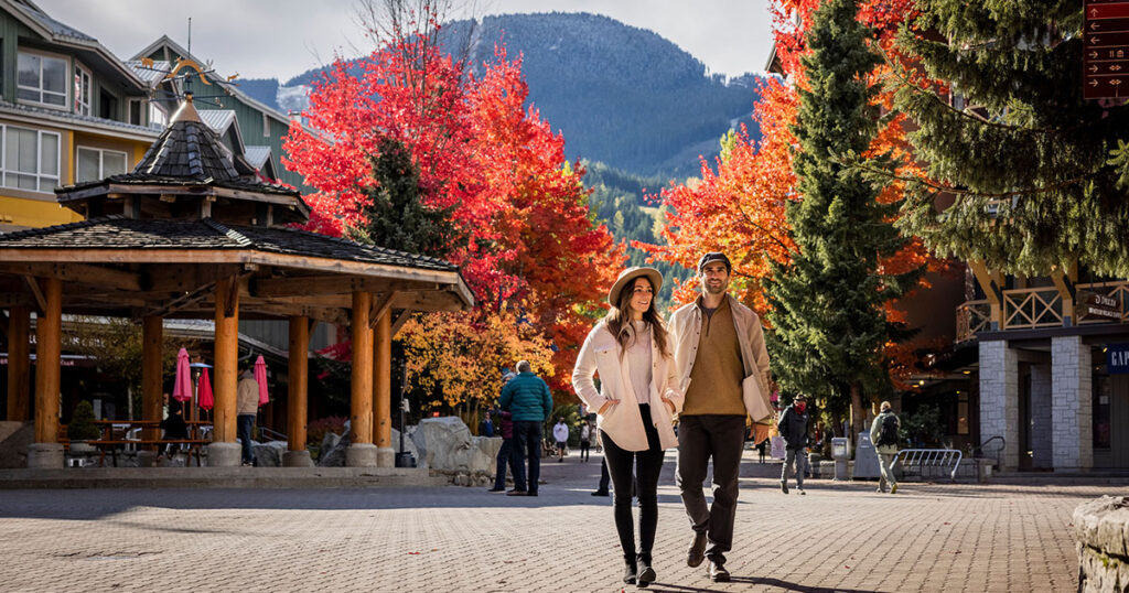 A couple walk through the Whistler Village Stroll with the fall colours around them.
