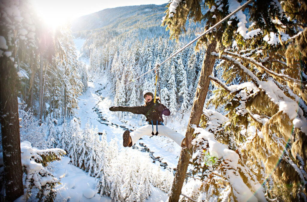 A woman ziplines across the Whistler Valley in the snow.