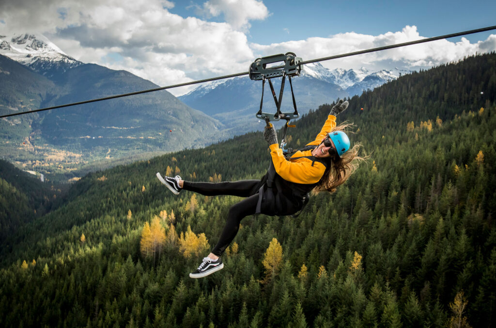 A woman ziplines across the mountains in Whistler in the beauty of fall.