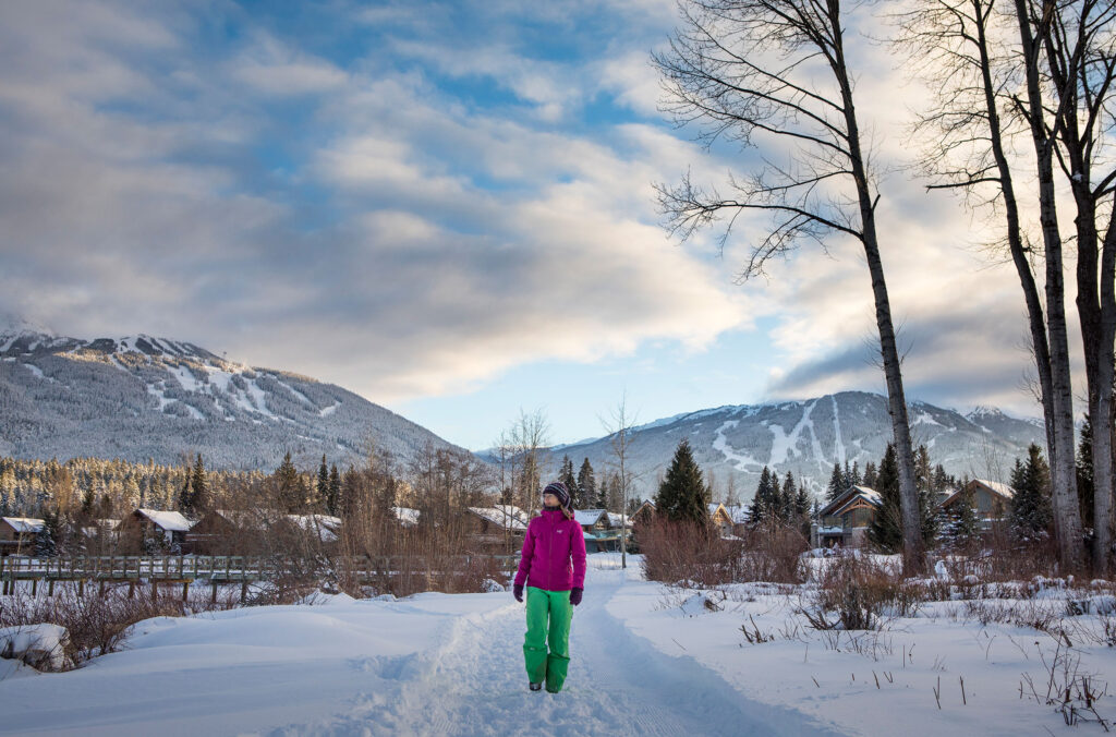 A woman walks in the snow in Whistler enjoying views of the mountains surrounding her.