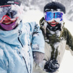 Two skiers smile at the camera covered in snow as they ski a powdery run on Whistler Blackcomb.