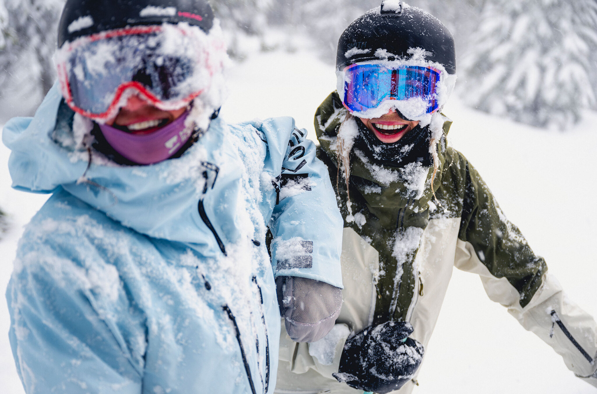 Two skiers smile at the camera covered in snow as they ski a powdery run on Whistler Blackcomb.