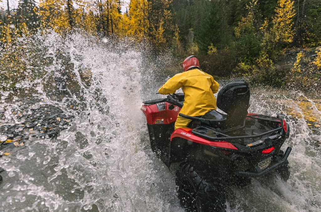 A person wearing full waterproof gear charges through a huge puddle on an ATV in Whistler.