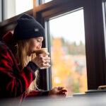 A woman drinks a coffee overlooking Blackcomb Mountain at Cranked Coffee in Rainbow, Whistler.