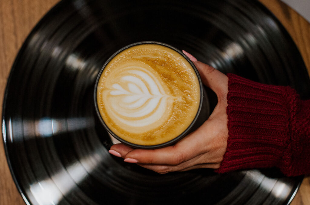 A woman holds a coffee with heart-shaped foam art over a record player disc at Rockit Coffee Co. in Whistler Creekside.