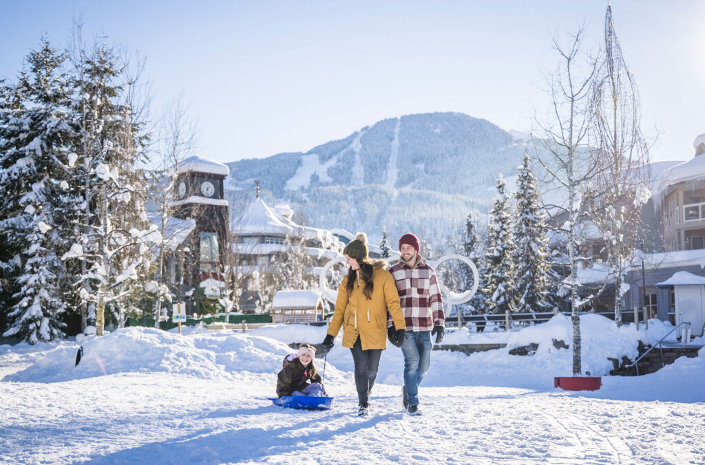 A couple pull a child on a sled at Olympic Plaza in Whistler Village.