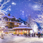 Whistler Village stroll with all its festive lights sparkling in the evening while snow falls.