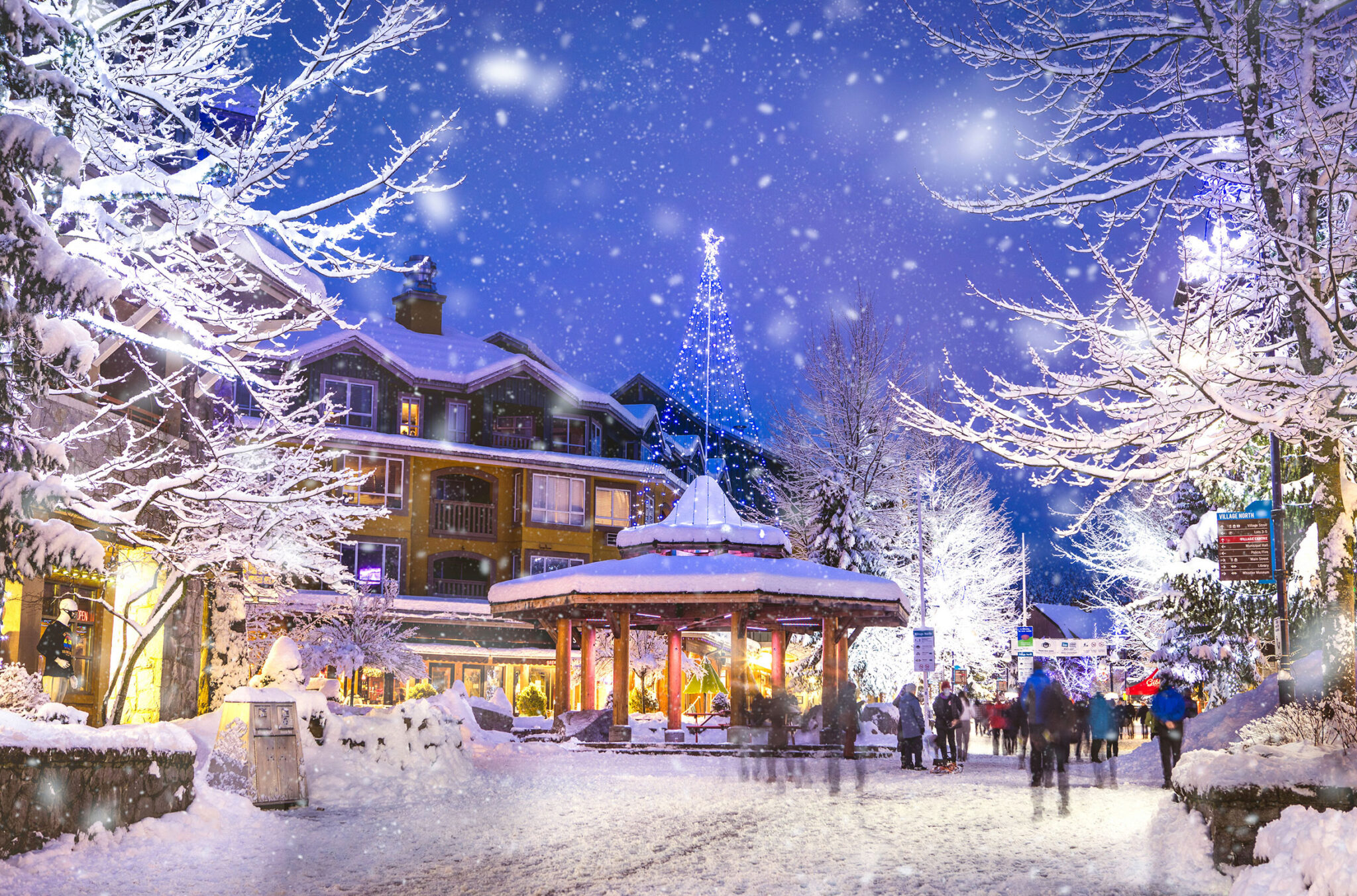 Whistler Village stroll with all its festive lights sparkling in the evening while snow falls.