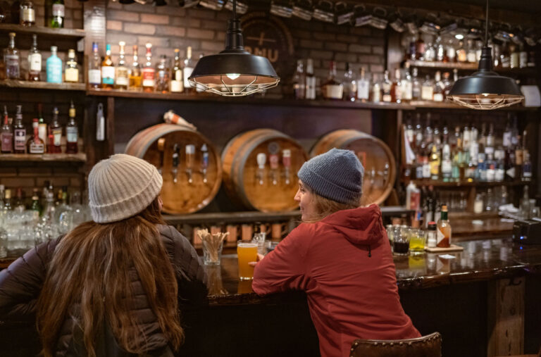 Two women sit at the bar at RMU Blackcomb enjoying an après craft beer.
