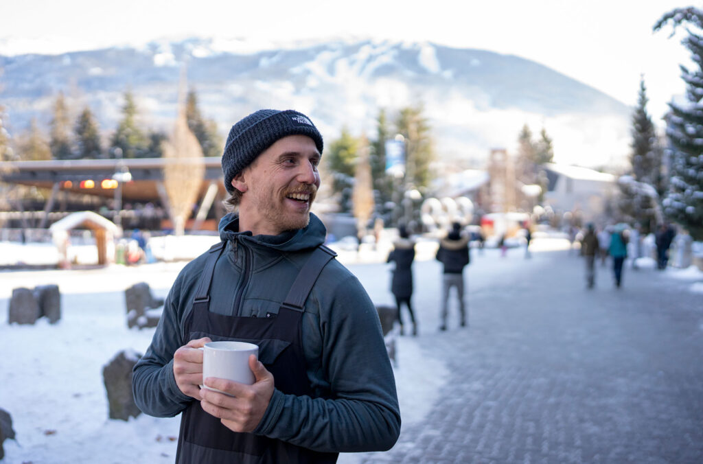 A man enjoys a hot chocolate from Blenz while looking out over Whistler Olympic Plaza.