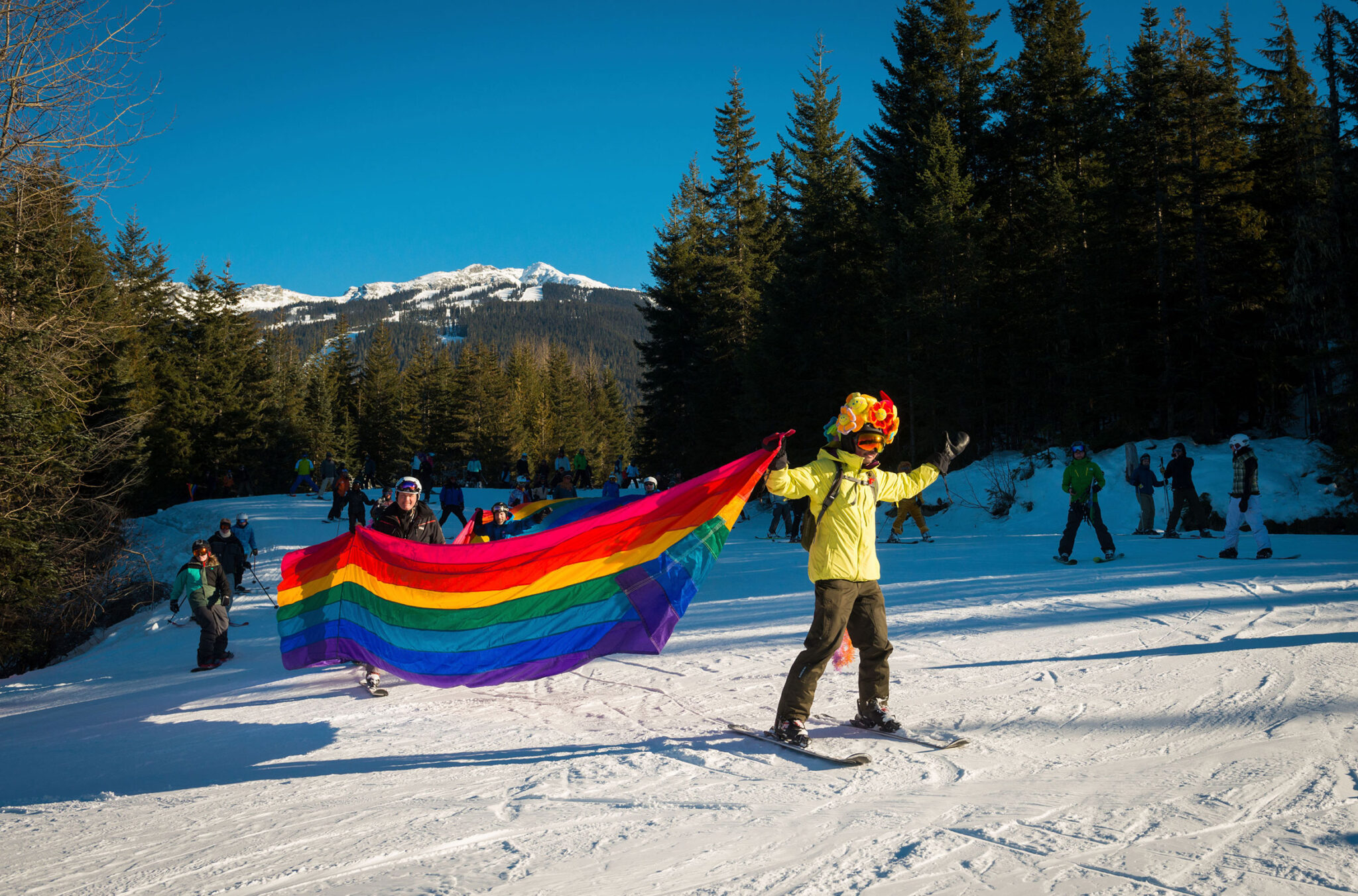 A skier with a balloon headdress makes their way down Whistler Blackcomb's slopes carrying a long rainbow flag to celebrate PRIDE in Whistler.