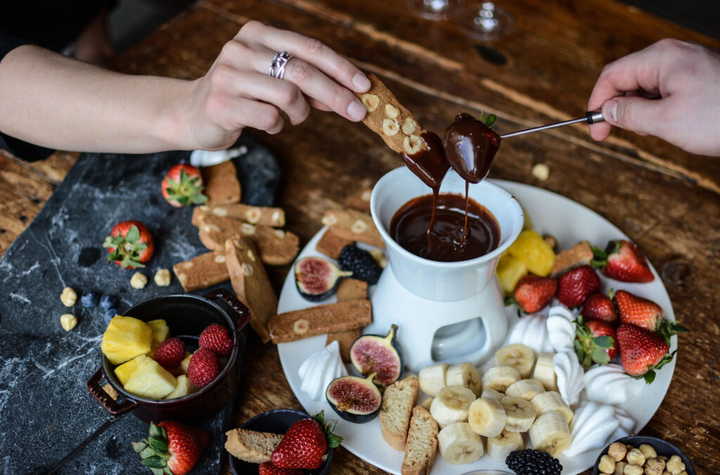 Hands dip biscotti and strawberries into a rich, decadent fondue at The Chalet in Whistler.