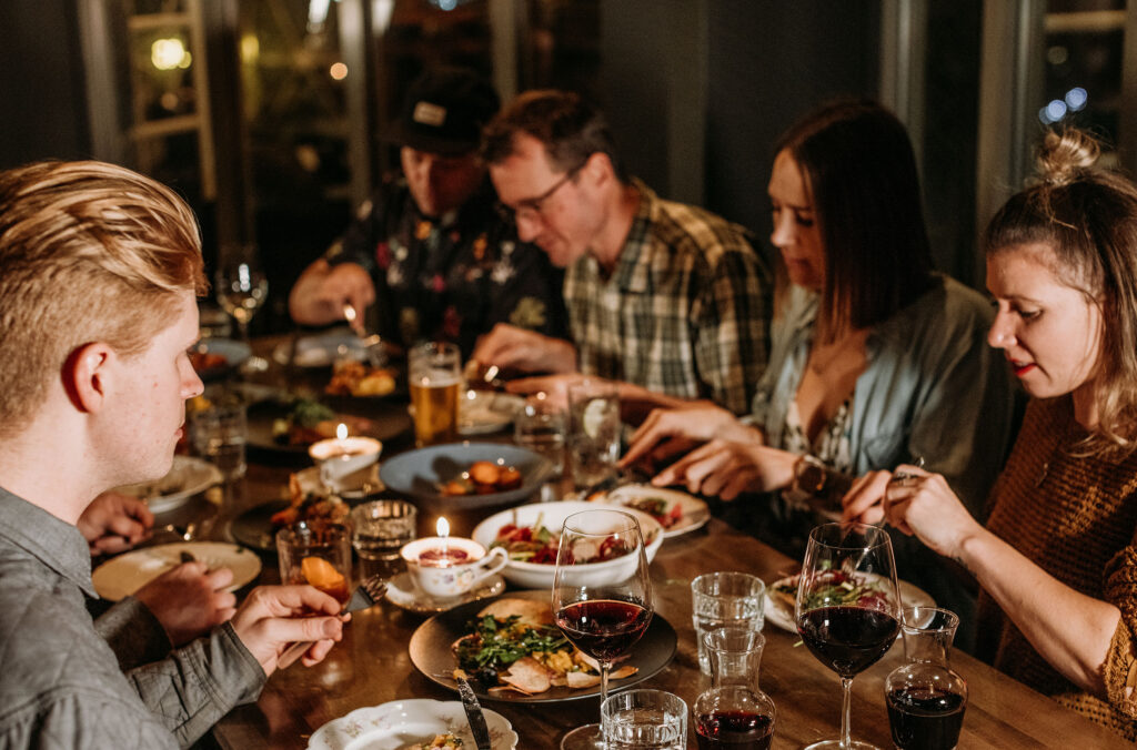 A group of friends dine at The Raven Room in Whistler, it looks warm and inviting with plates of good-looking food and full wine glasses.