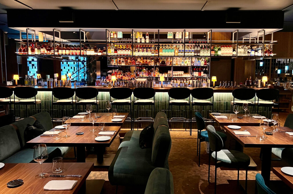 A shot of the dining room at Wild Blue with its walnut wood and dark blue velvets are the forefront.