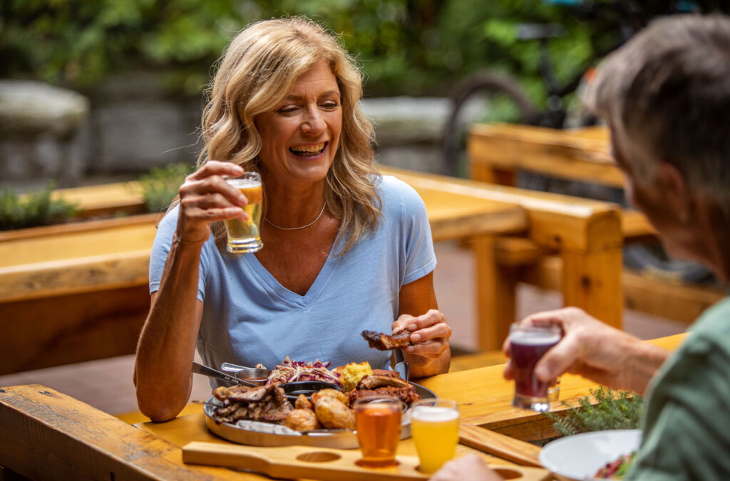 A man and woman share food with beers outside on the patio at Hunter Gather in Whistler.
