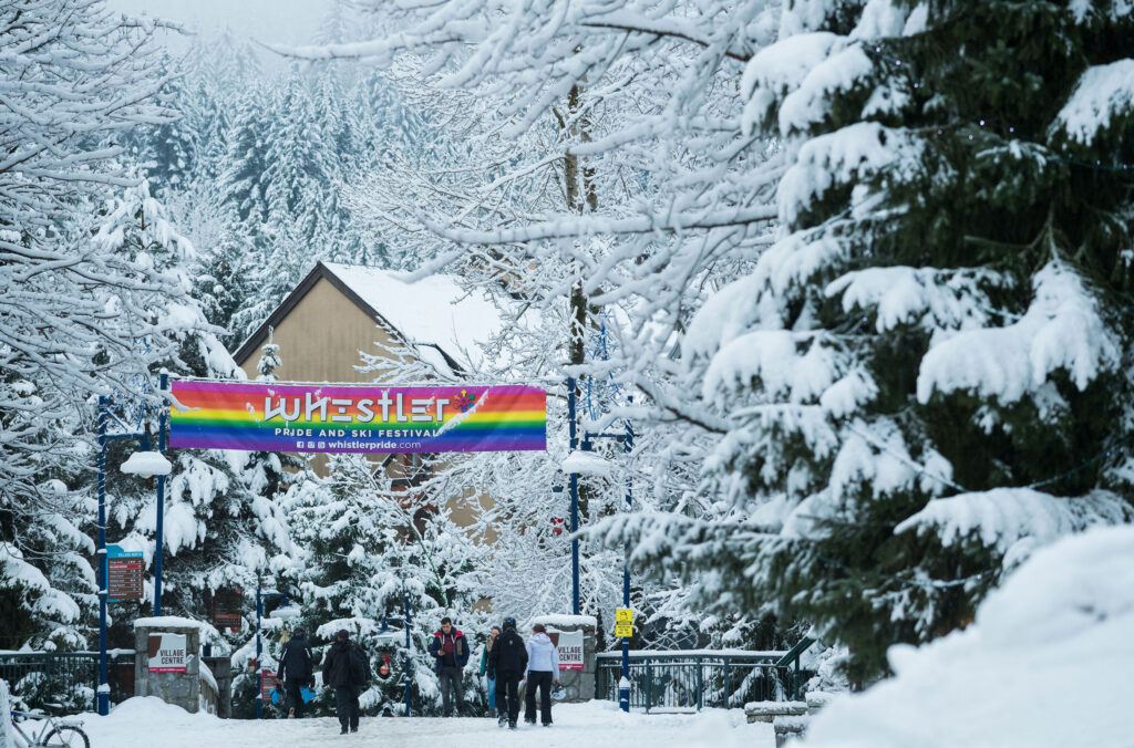 A shot of the rainbow, festival banner above the streets of a snowy Whistler Village.