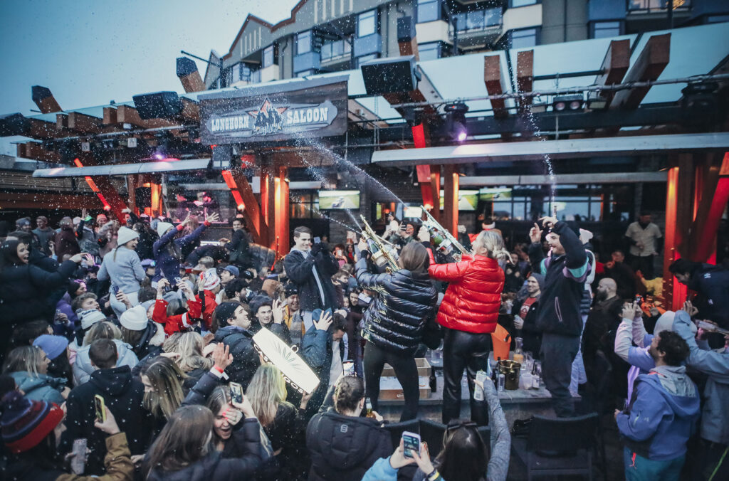 Two women stand on tables on the Longhorn patio firing champagne guns into a patio full of people dancing.