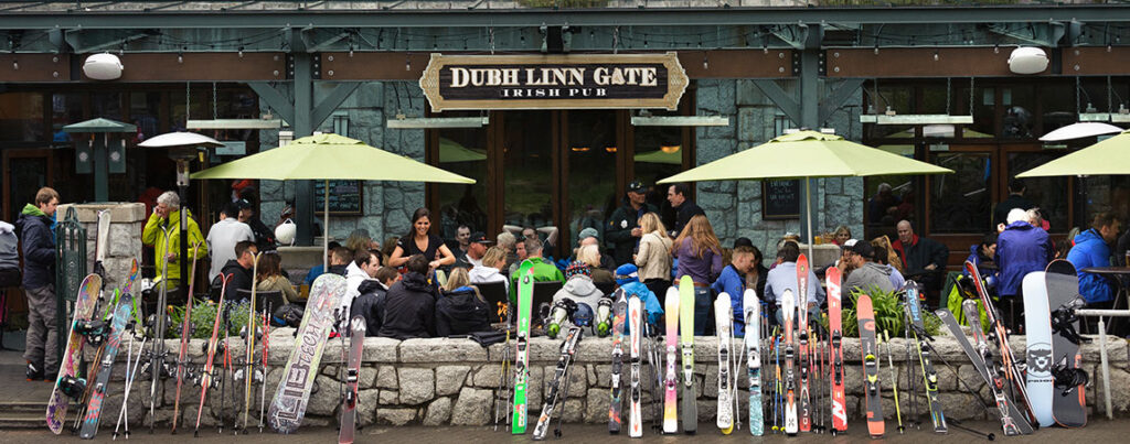 Skis and snowboards line the walls of the Dubh Linn Gate's patio with people enjoying apres around fires and patio heaters.