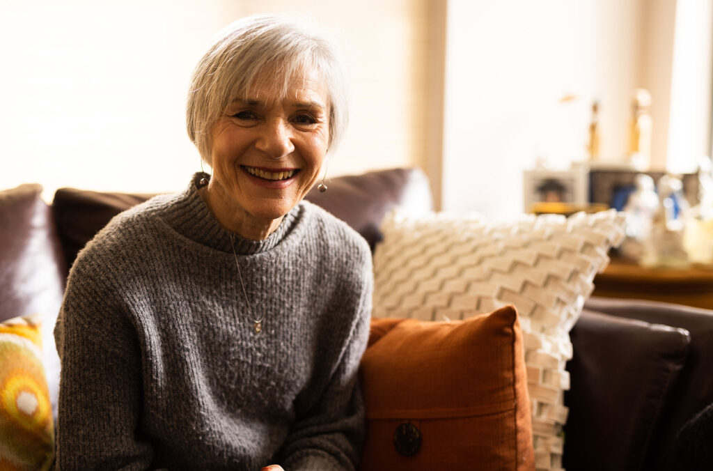 Brenda Baker looks directly at the camera sat on her living room sofa.