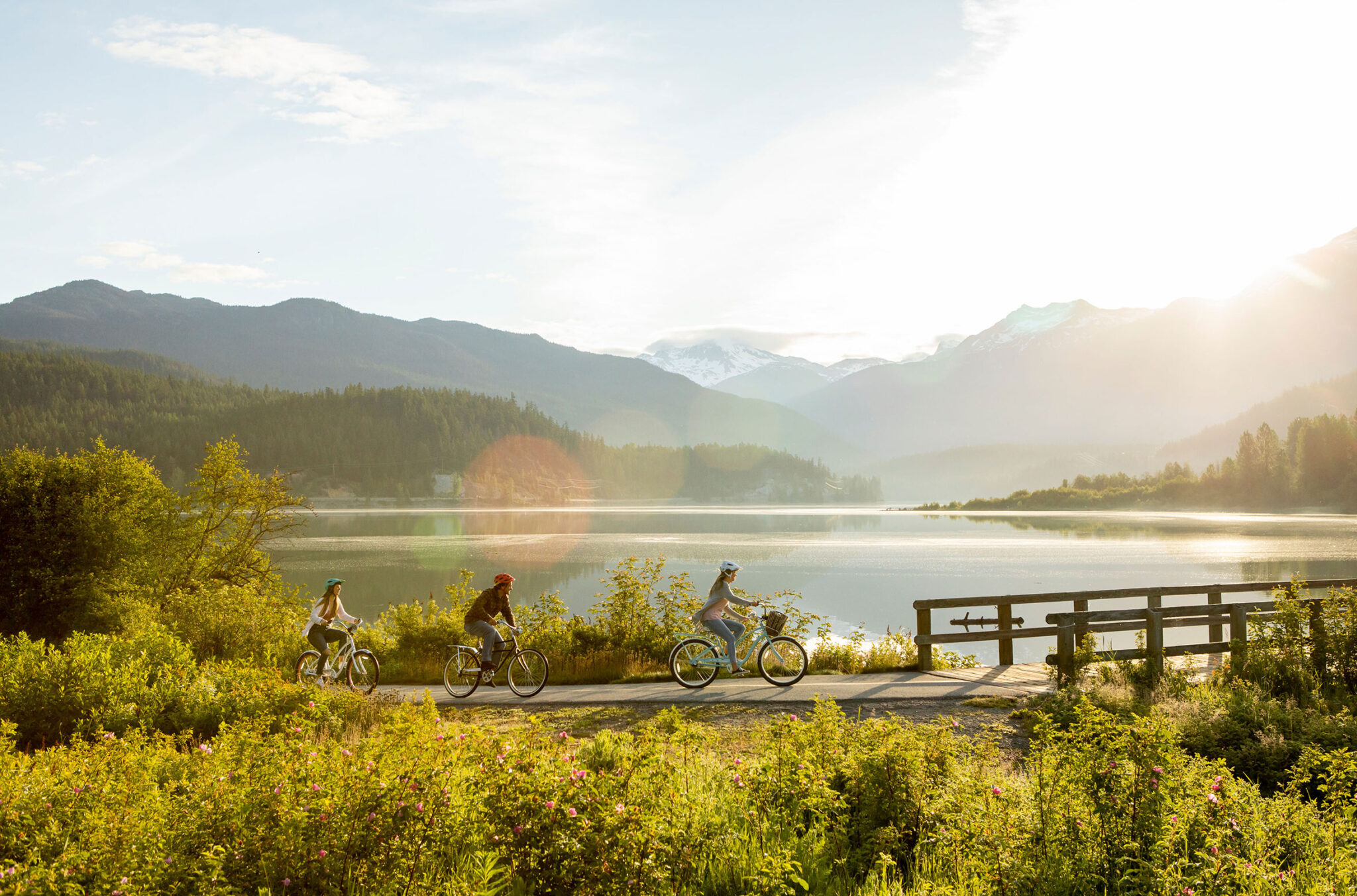 Three cyclists ride in the spring sunshine along the Valley Trail around Green Lake in Whistler.