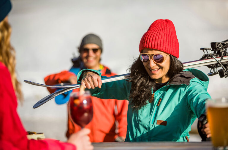A woman carries her skis over her shoulder as she makes her way to apres in the spring sunshine.