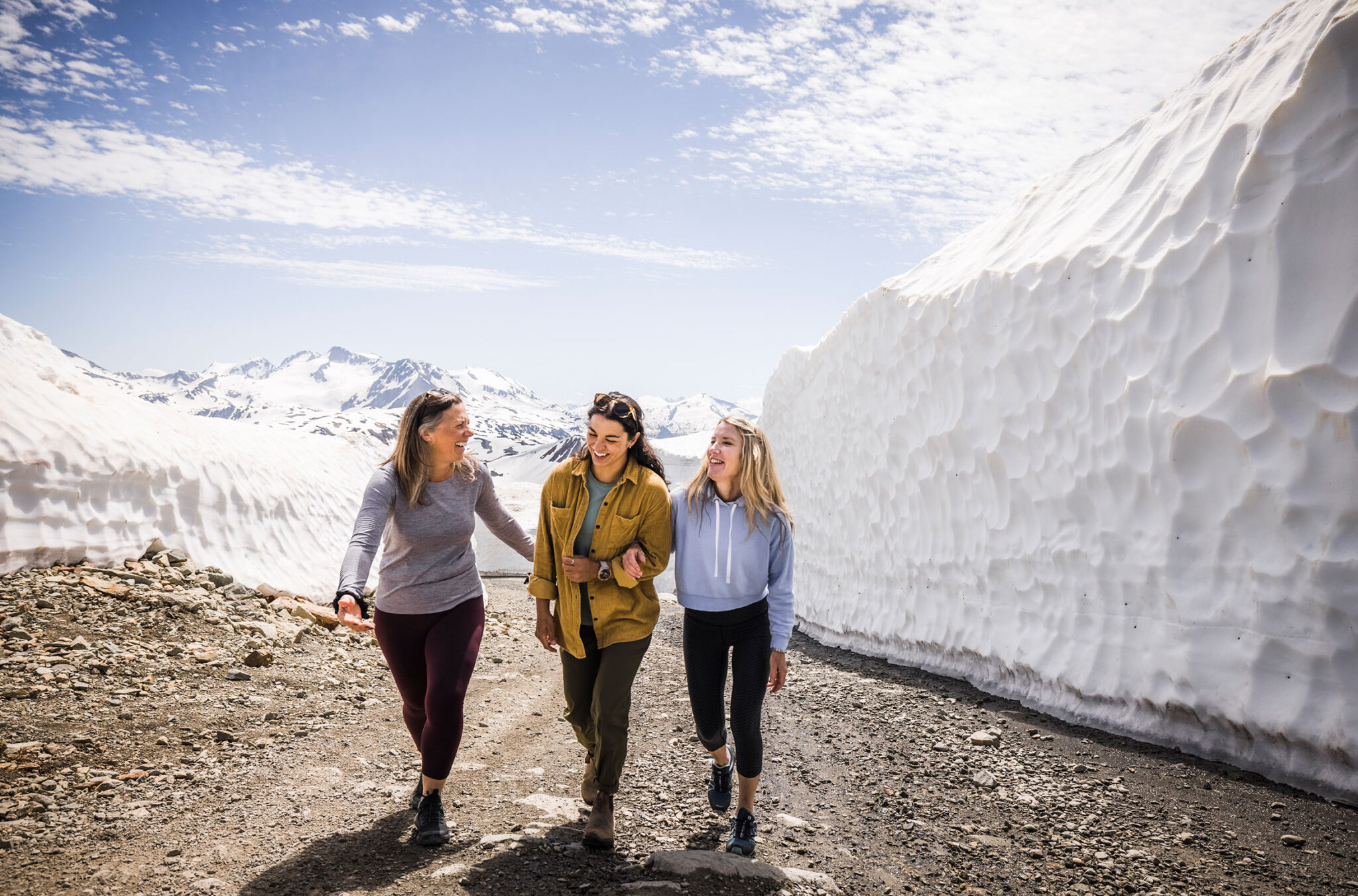 Three women walk up Whistler Mountain amongst the snow walls in the early summer.