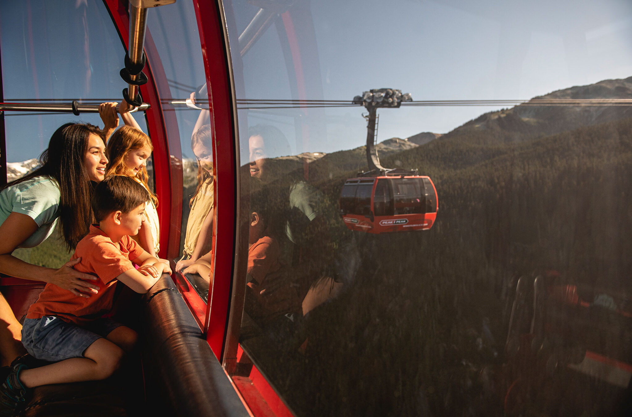 A family looks out at the view from the PEAK 2 PEAK Gondola in Whistler with the summer sun shining in.