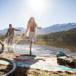 A man and woman splash along the shores of a lake in Whistler after getting off their bikes.