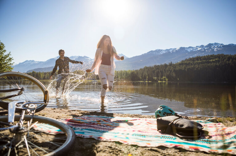 A man and woman splash along the shores of a lake in Whistler after getting off their bikes.
