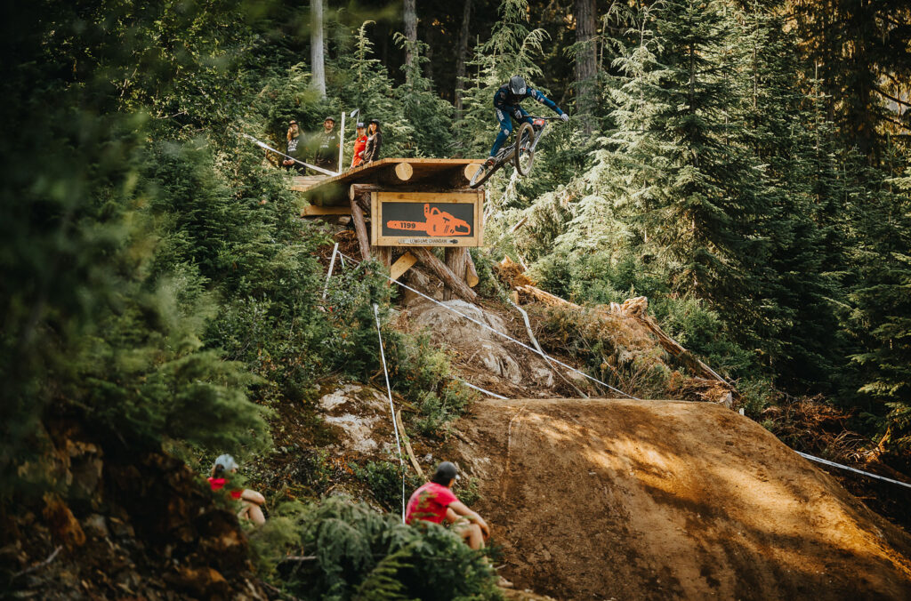 A bike rider goes over a large wooden drop on the downhill course during Crankworx Whistler.