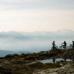 Three mountain bikers get ready to go in the high alpine with the Coast Mountains in the background.