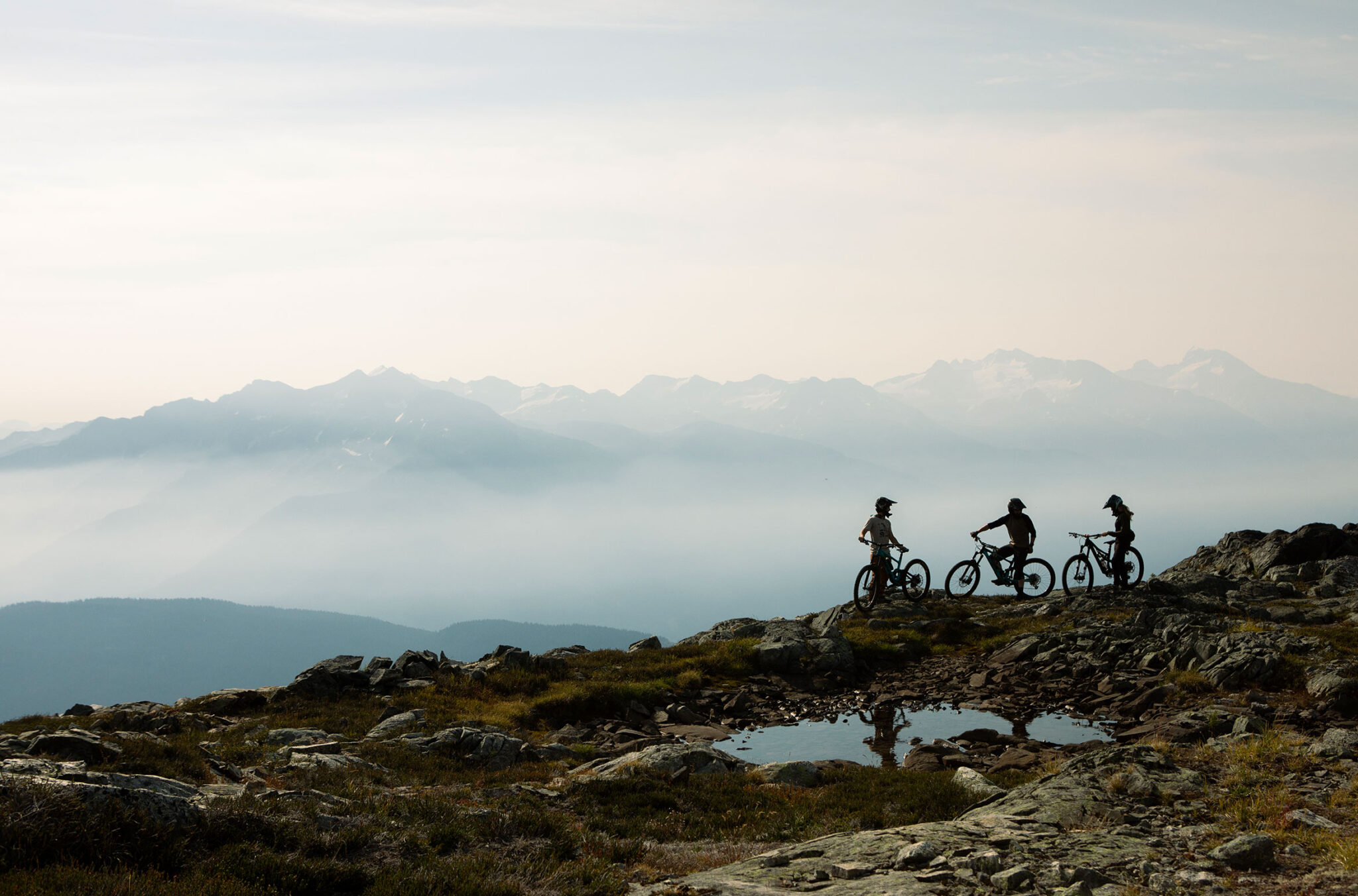 Three mountain bikers get ready to go in the high alpine with the Coast Mountains in the background.